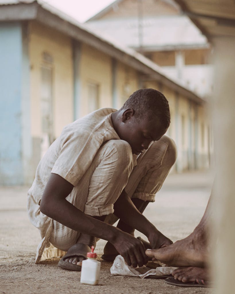 A young boy is sitting on the ground and putting on his shoes