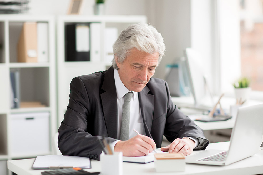 A man sitting at a desk looking at a laptop